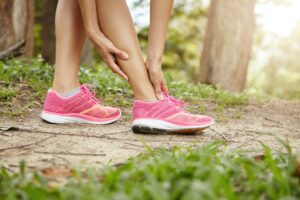 Running sport injury. Female athlete jogger wearing pink sneakers touching her twisted or sprained a